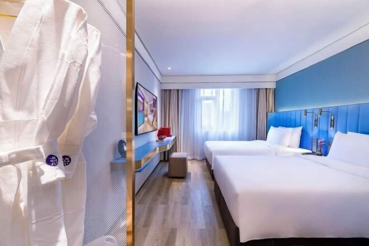 Habitación de hotel con dos camas, un escritorio, una silla y un televisor.