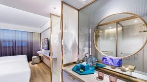 A modern hotel room with a bed, a vanity with a mirror, and a bathroom with a shower.