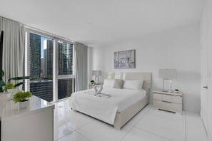 A modern hotel room with a large bed, a desk, and a view of tall buildings. - Icon Brickell 2BR | Poolside Paradise in the Sky (Miami)