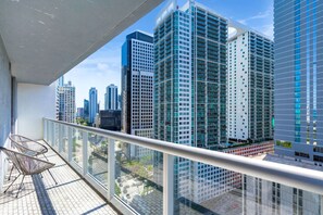 A balcony with a view of high-rise buildings, a chair, and a glass railing. - Icon Brickell 2BR | Poolside Paradise in the Sky (Miami)