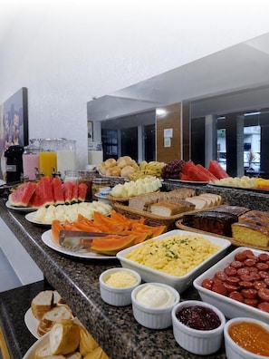 Un buffet proposant une variété d’aliments, notamment des fruits, du pain et des pâtisseries.