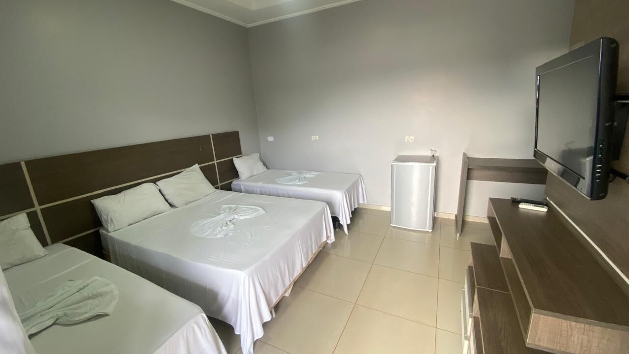 Une chambre d’hôtel avec trois lits, une télévision, une petite table et un réfrigérateur.