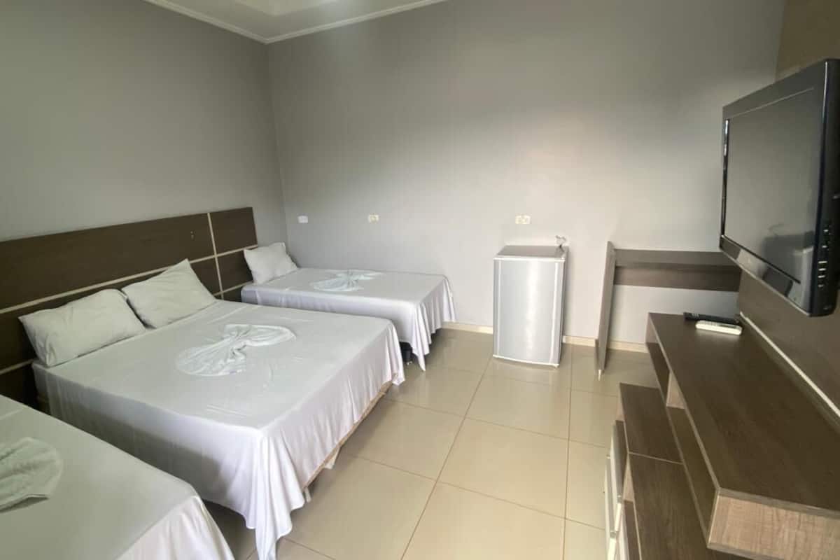 Een hotelkamer met drie bedden, een televisie, een kleine tafel en een koelkast.