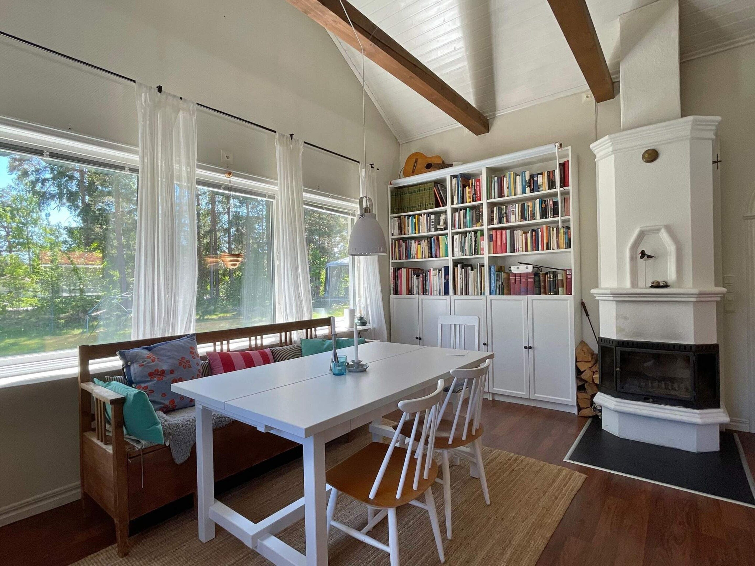 Una habitación acogedora con una mesa blanca, sillas, una estantería y una chimenea.
