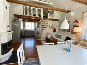 Ett rymligt vardagsrum med en öppen spis, ett matbord och en trappa som leder upp till en övre våning.