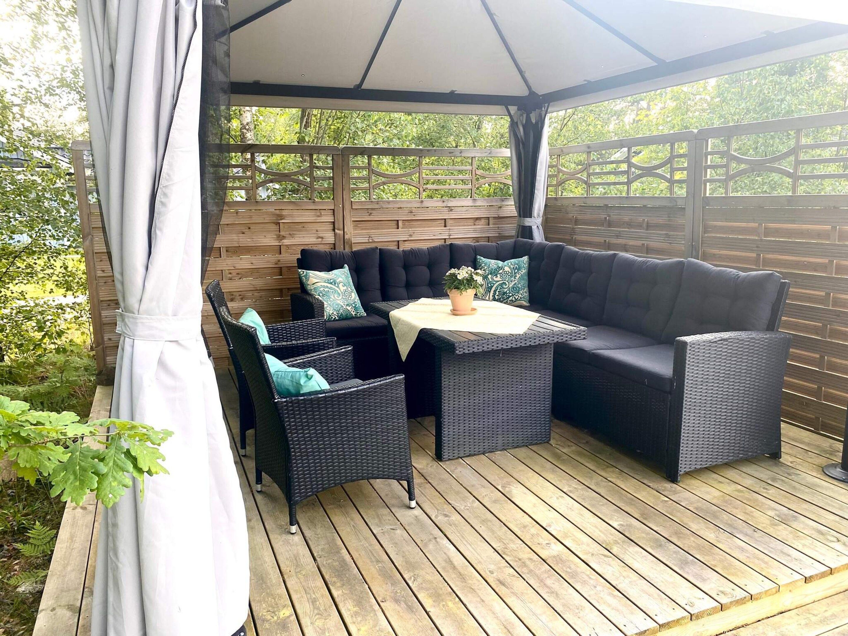 Une terrasse extérieure dotée d’un espace salon couvert, comprenant un canapé et des fauteuils, une table et une plante en pot.