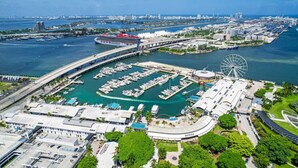 A marina with boats, a large Ferris wheel, and a bridge connecting to a city skyline. - Bayview 2BR Retreat | Stunning Views + Pool (Miami)