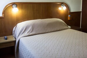 A hotel room with a wooden headboard, two bedside lamps, a bed with a patterned bedspread, and a nightstand with a remote control. - Orly Hotel (Corrientes)