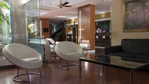 Een moderne lobby met twee witte stoelen, een glazen salontafel en een zwarte bank.