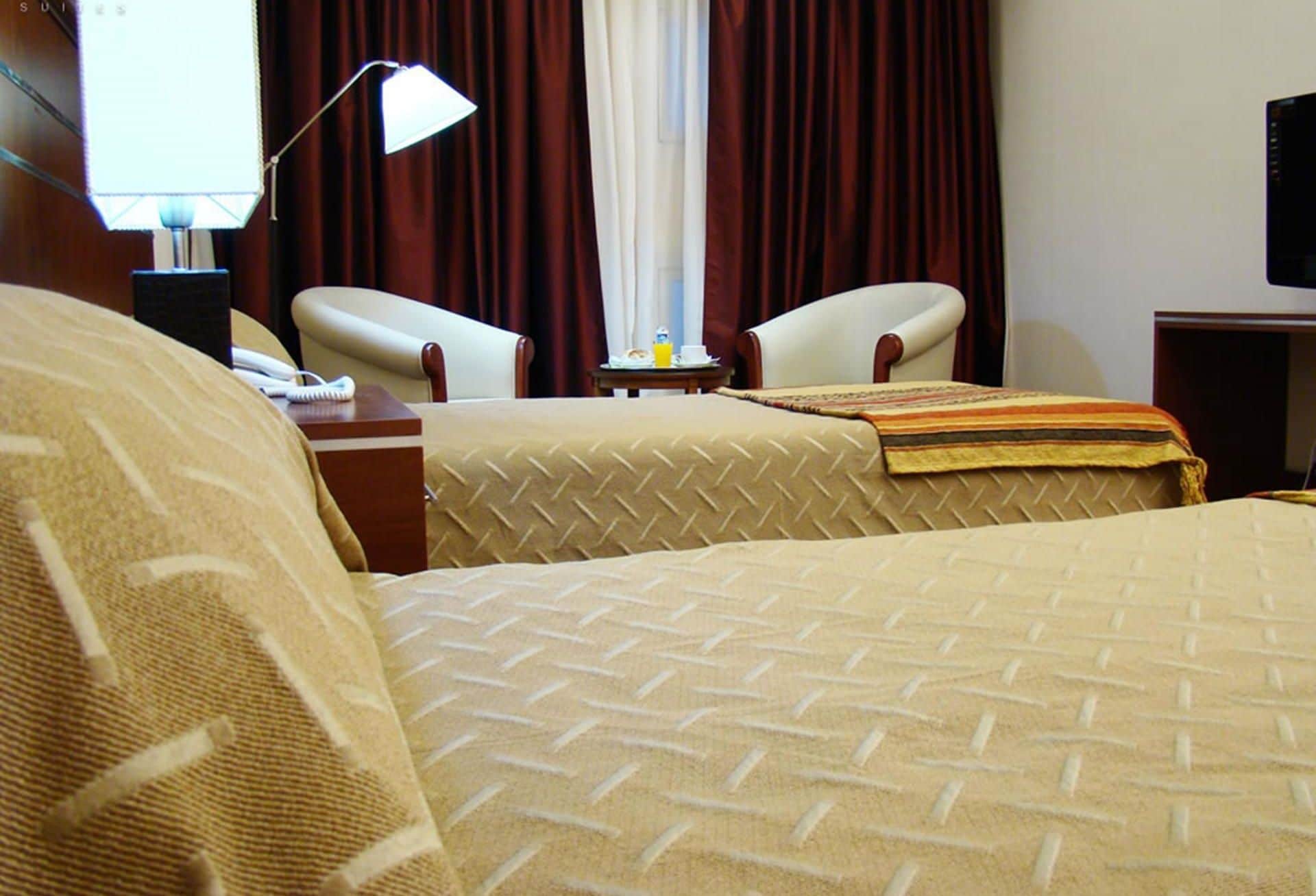 A hotel room with two beds, a desk with a lamp, a chair, and a television.