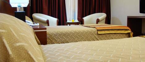 A hotel room with two beds, a desk with a lamp, a chair, and a television.