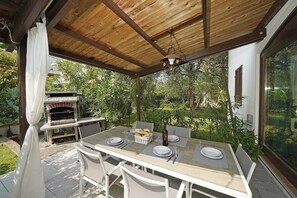 An outdoor patio with a wooden ceiling, a pizza oven, and a dining table set for two. - La casa della Bougan-ville (Toscolano-Maderno)