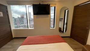 A hotel room with a bed, a TV mounted on the wall, a large window with a city view, and a mirror. - SAANA Living & Hotel Downtown Bogota (Bogota)