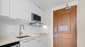 Una cocina con armarios blancos, un lavamanos de acero inoxidable y un microondas.