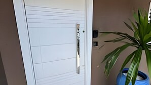 Une porte blanche avec une poignée, un paillasson jaune orné de flèches indiquant la direction, et un vase bleu avec des feuilles vertes.