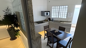Une cuisine moderne avec des meubles blancs, un four à micro-ondes et une fenêtre équipée de stores.