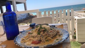 A table with a plate of pasta, a blue bottle, and a view of the ocean.