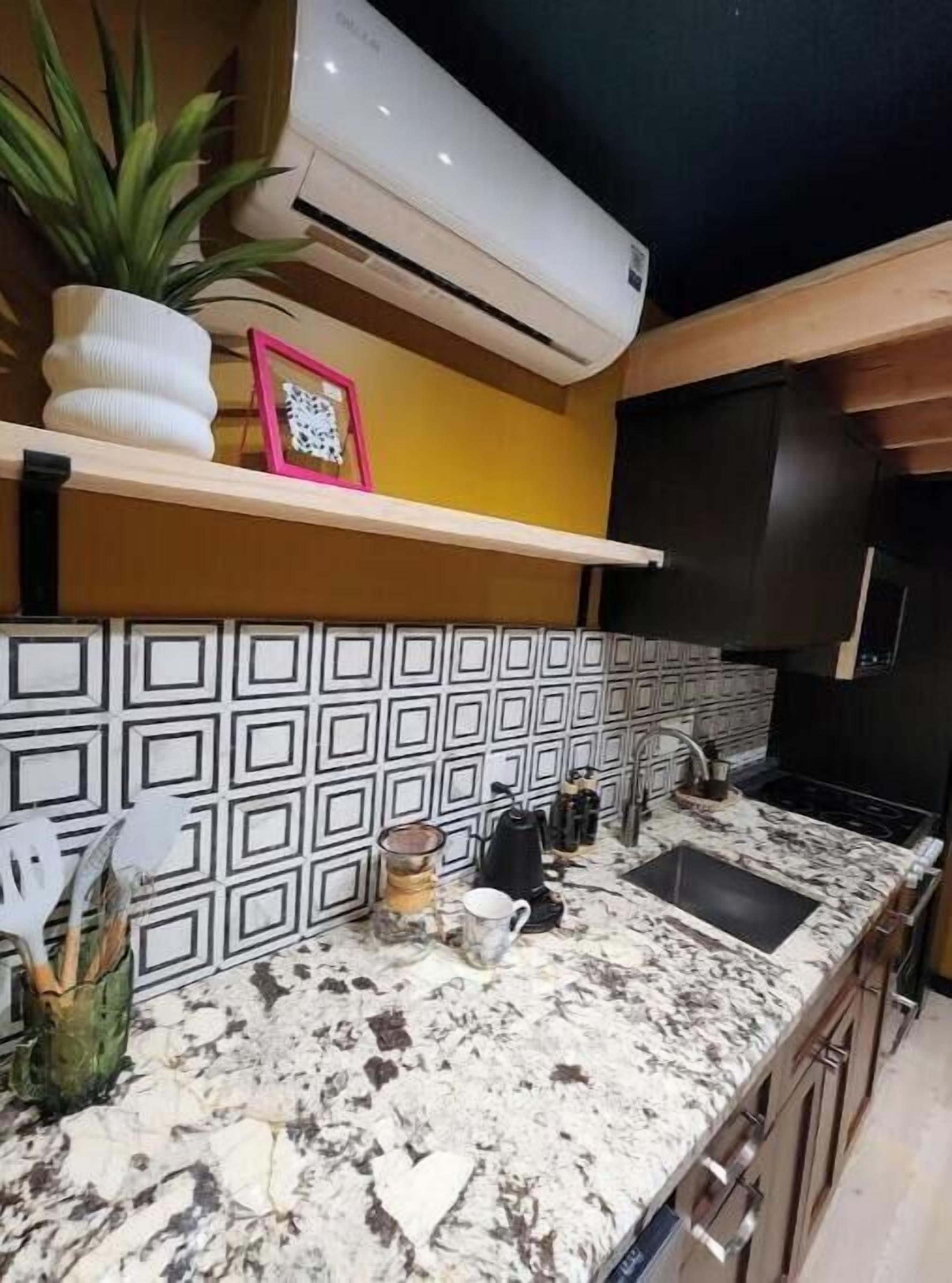 A kitchen with a marble countertop, a black sink, and a patterned backsplash.