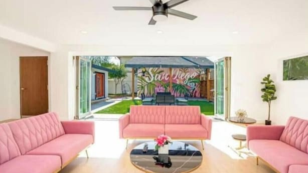 A modern living room with a pink sofa, a glass coffee table, and a ceiling fan. - Sunny Villa Lake Trails Beach (La Mesa)
