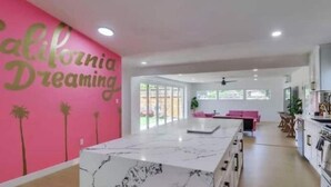 A spacious kitchen with white cabinets, a marble countertop, and a bright pink accent wall with palm tree decorations. - Sunny Retreat Beaches Lakes Trails (La Mesa)
