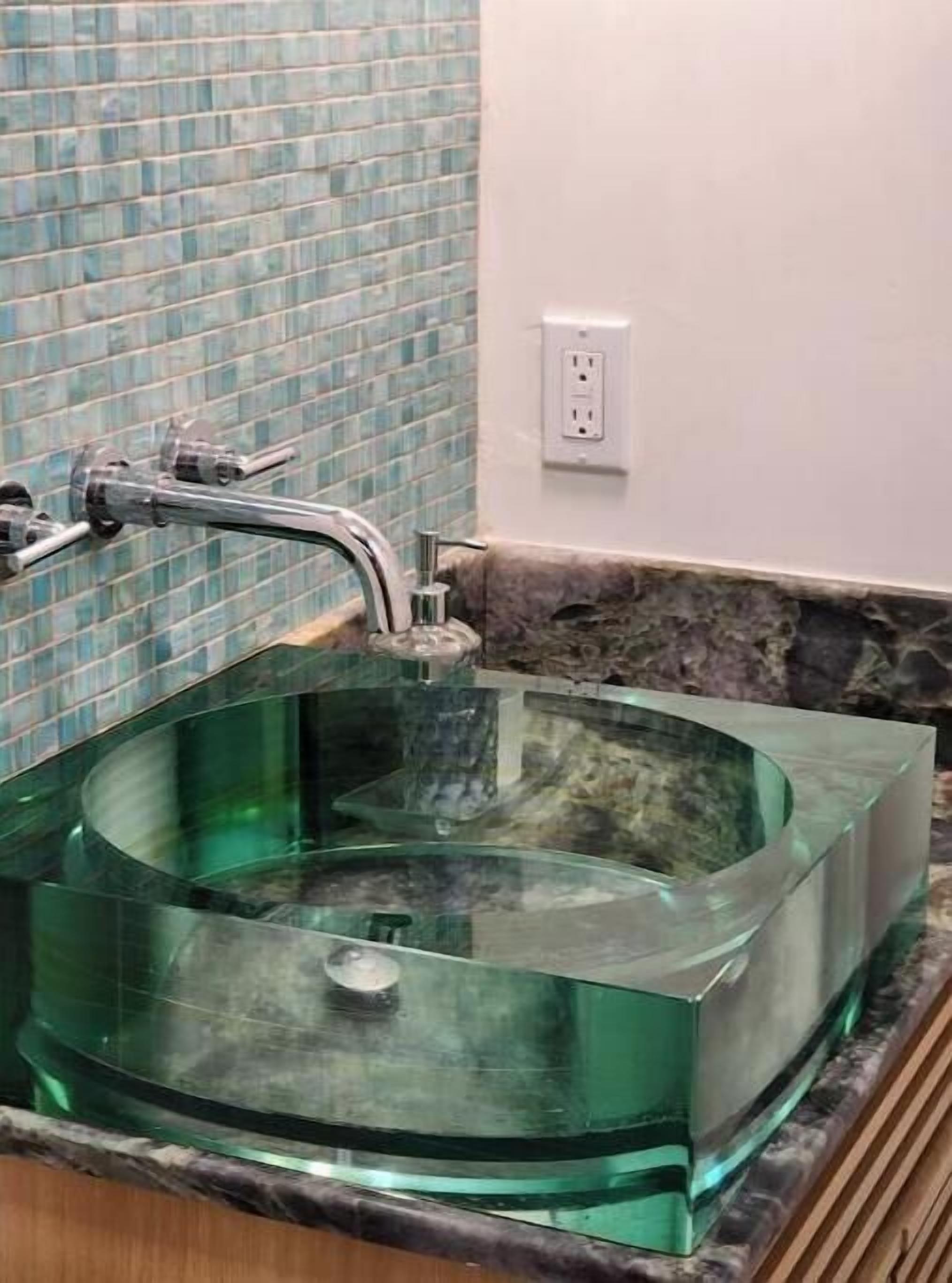 Un baño moderno con lavamanos de vidrio, salpicadero de azulejos y encimera de mármol.