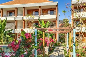 A multi-story hotel with balconies, a garden area with pink flowers, and a clear sky. - Sanur Lodge (Bali)