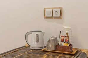 A kitchen area with a kettle, a coffee maker, a jar of sugar, and a tray with a mug and a box labeled 'PUSKELAPA.' - Sanur Lodge (Bali)
