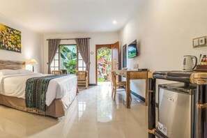 A hotel room with a bed, a desk, a television, and a refrigerator. - Sanur Lodge (Bali)