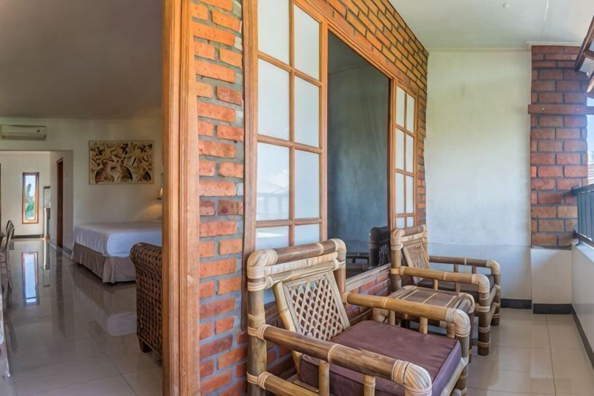 A room with a brick wall, a large window, wicker furniture, and a bed.