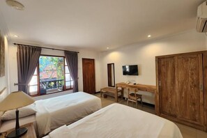 A hotel room with two beds, a desk, a television, and a wardrobe. - Sanur Lodge (Bali)