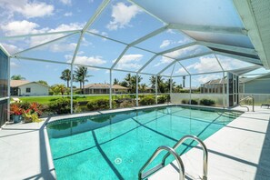 A clear blue pool with a metal roof structure, surrounded by a white tiled deck and potted plants.