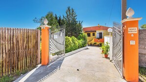 A gated entrance to a building with a wooden fence and metal gates, leading to a yellow building with a red roof.