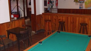 Une table de billard avec quatre tabourets, un coin bar également équipé de tabourets, et une porte donnant sur une autre pièce.