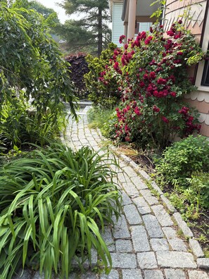Un sendero de piedra que conduce a una casa rodeada de exuberante follaje y plantas florecientes.