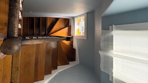 Eine Treppe mit Holzbodenstufen führt zu einer Zwischenebene, ein Fenster mit Jalousien und eine Wand mit strukturierter Oberfläche.
