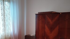 A bedroom with a bed, a wooden wardrobe, and a window with curtains.