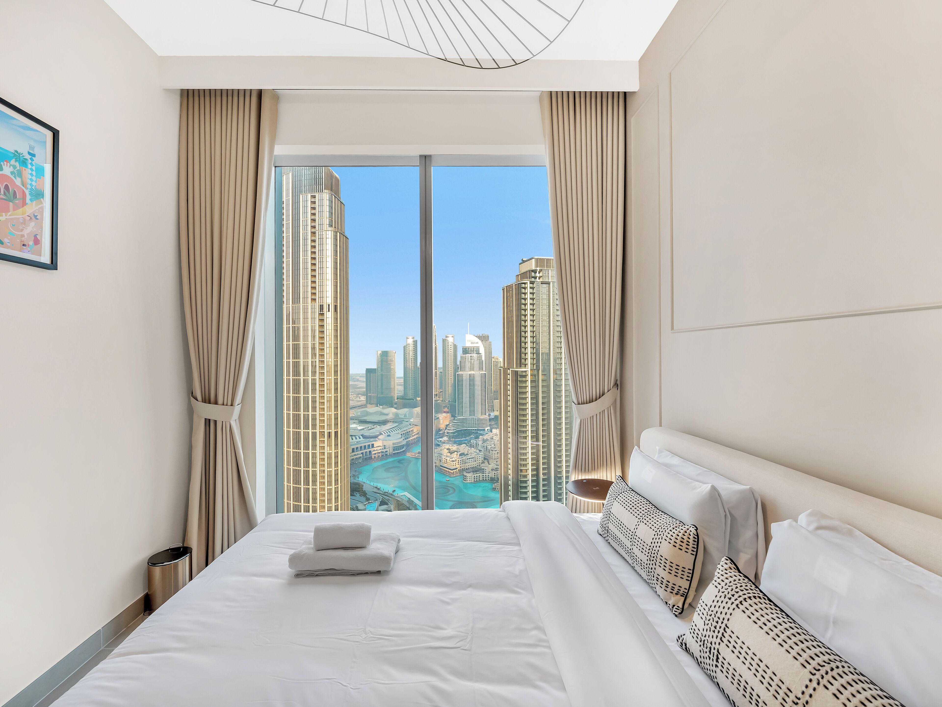A modern hotel room with a large bed, a view of tall buildings, and a framed picture on the wall.