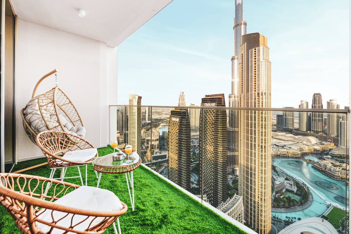 Un balcon avec un fauteuil suspendu, une petite table et une vue sur le Burj Khalifa et les bâtiments environnants.