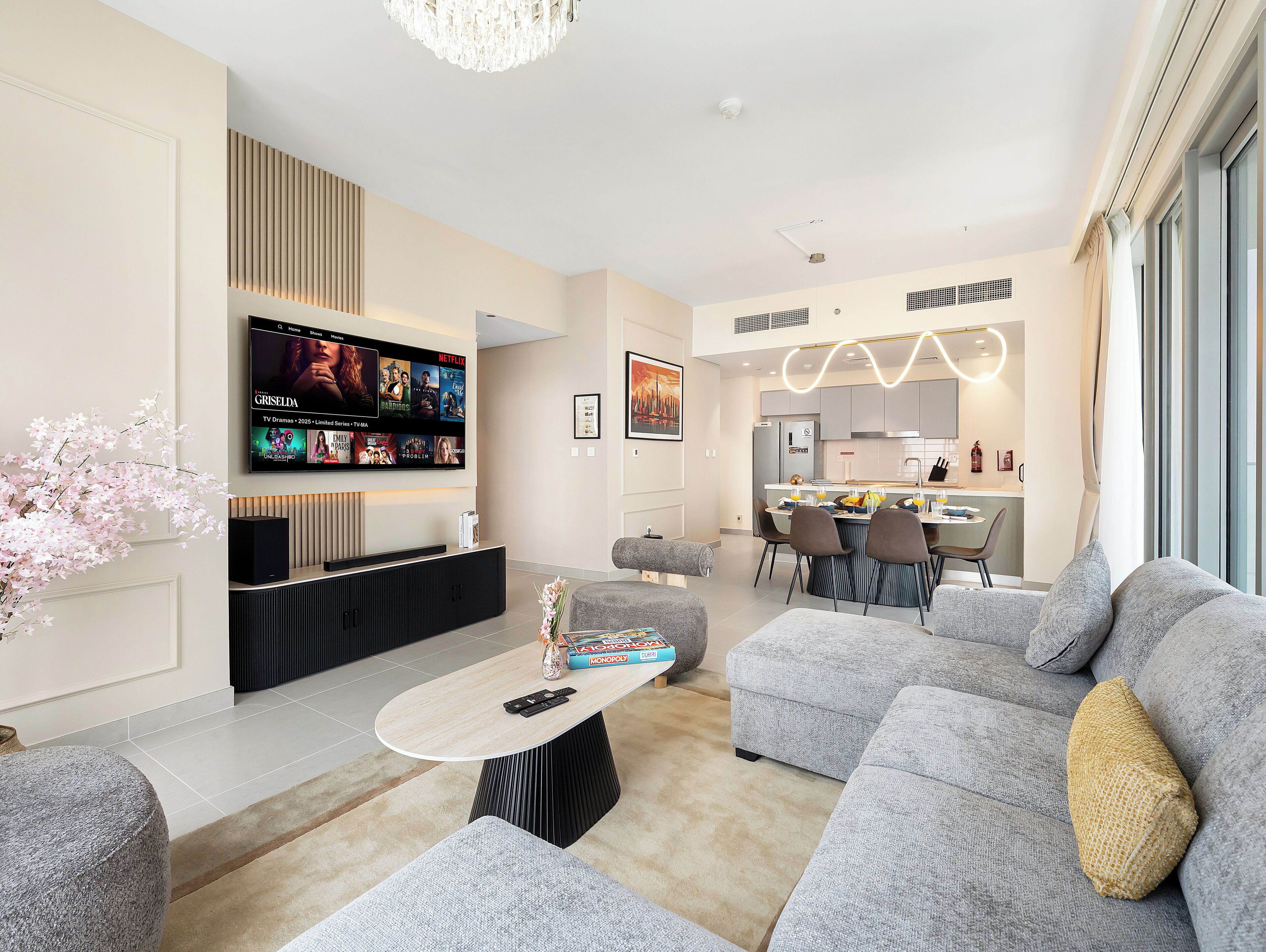 Een moderne woonkamer met een flatscreen televisie, grijze banken, een salontafel en een keuken op de achtergrond.