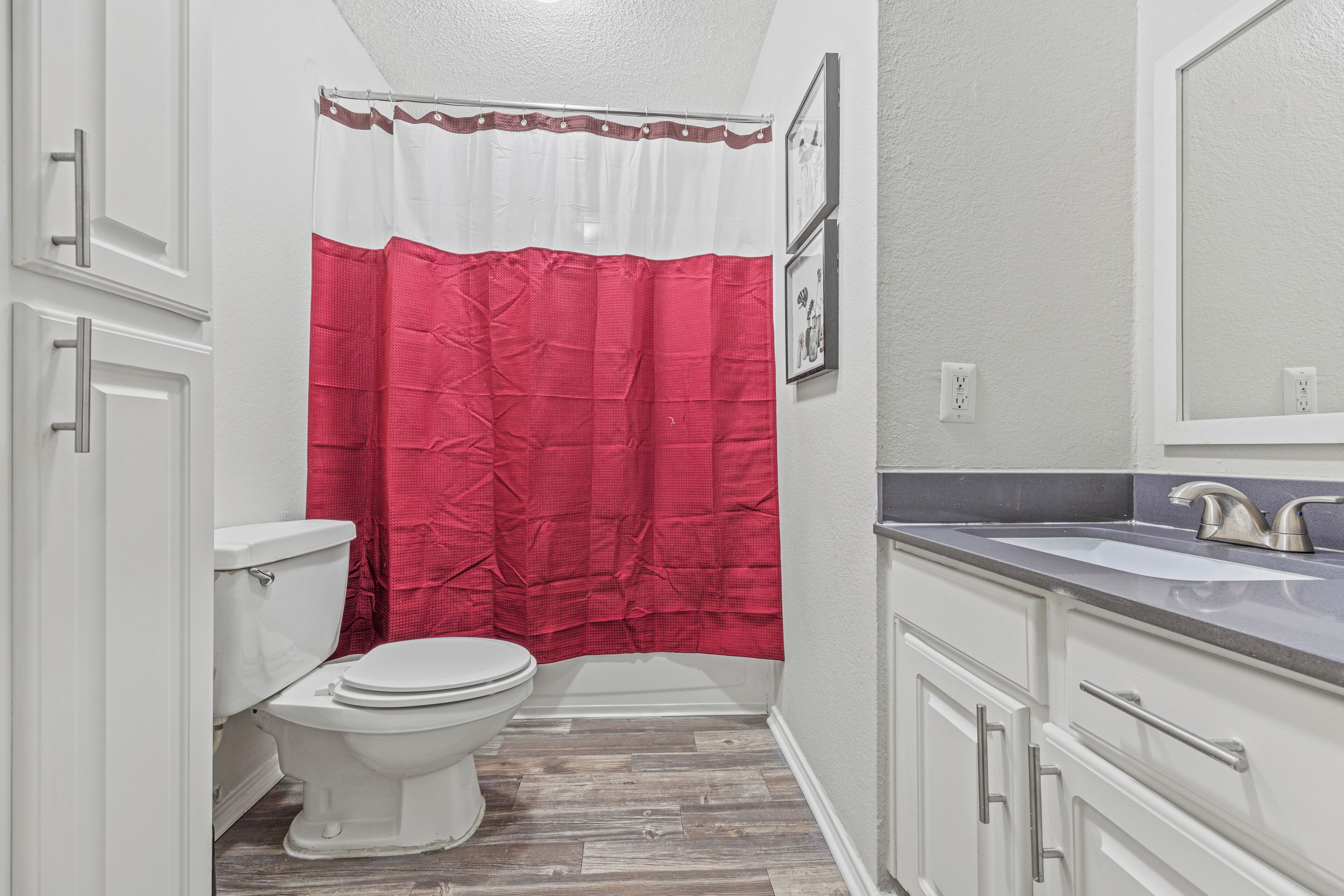 A bathroom with a white toilet, a red shower curtain, and a sink with a mirror above it.