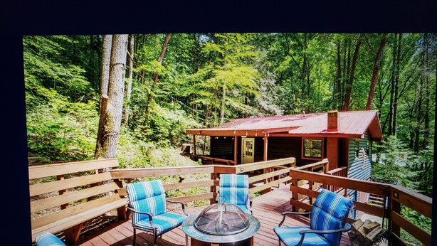 A deck with outdoor furniture and a fire pit, surrounded by a forest. - Charming 2-bedroom cabin with WiFi, AC in enchanting Blairsville (Blairsville)