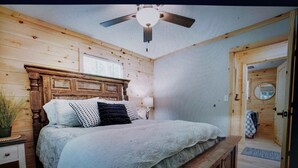 A bedroom with a wooden headboard, a bed with a white and gray bedspread, a ceiling fan, and a wooden door. - Charming 2-bedroom cabin with WiFi, AC in enchanting Blairsville (Blairsville)