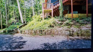 A cabin with a wooden deck, a staircase leading to a second level, surrounded by dense forest. - Charming 2-bedroom cabin with WiFi, AC in enchanting Blairsville (Blairsville)