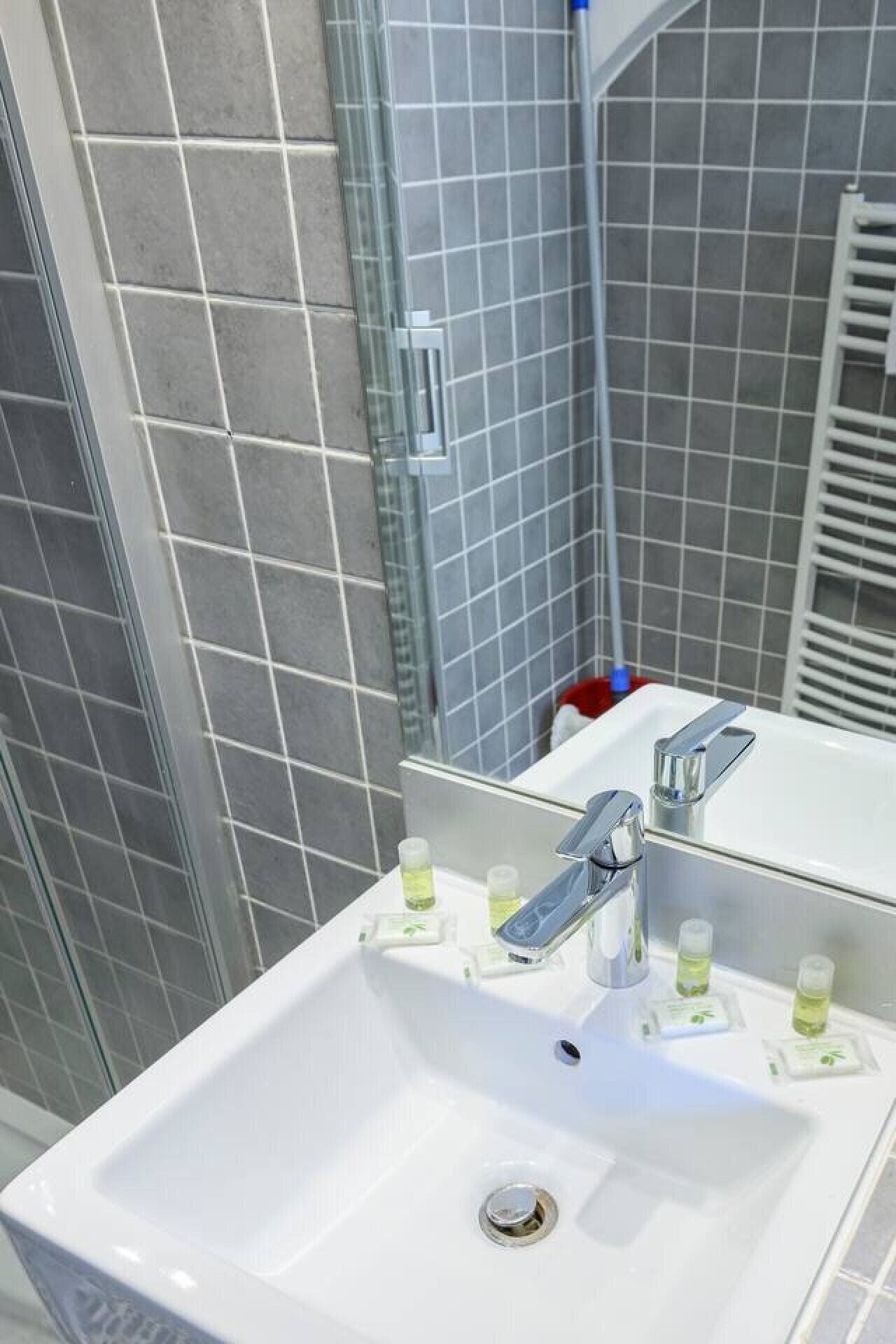 A bathroom with a white sink, a mirror, and a shower area with grey tiles.