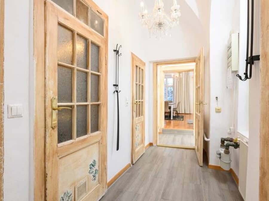 Un pasillo con puertas de madera, una araña y vista a otra habitación.