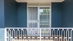A balcony with a white railing, a sliding glass door, and a view of a building with a fence. - Maryz Secret Haven, cozy one bedroom Air BnB Condo (Kampala)