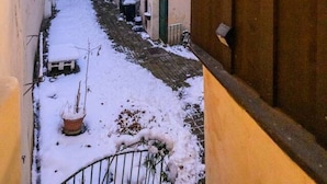 Een smalle steeg met een met sneeuw bedekte grond, begrensd door gebouwen met traditionele architectuur en een houten deur aan de rechterkant.