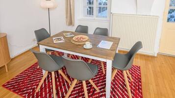 A dining area with a wooden table, grey chairs, and a red patterned rug.