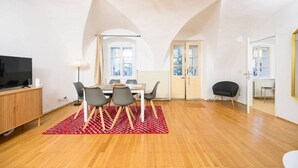 Een moderne woonkamer met een eethoek, houten vloeren en een groot raam dat voor natuurlijk licht zorgt.