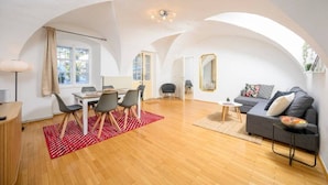 Een ruime woonkamer met een eettafel, stoelen, een bank en een bijzettafeltje.